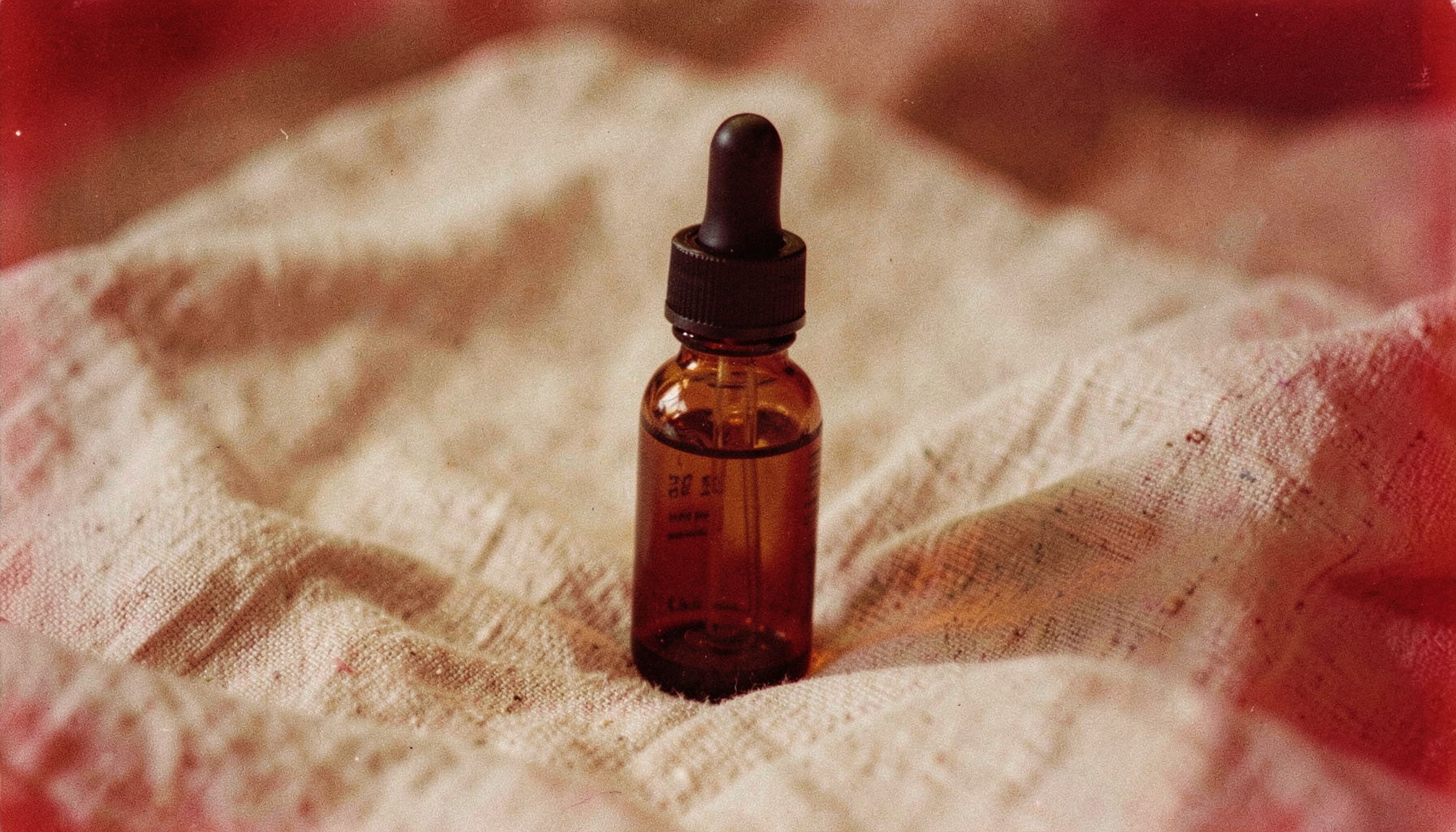 Close-up analog film image of a small amber glass bottle with a dropper cap resting on a linen cloth, warm earthy tones and soft grain